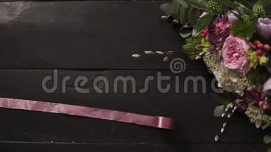 两条丝质的粉色缎带<strong>舒展</strong>在漆黑的木质表面，一束美丽的花束在一个框架内.. 慢动作